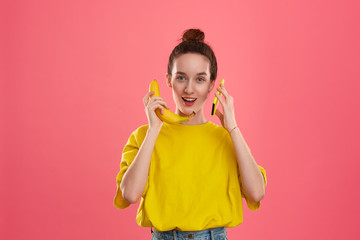 Smiling model with a hair bun in a yellow t-shirt holding banana speaking on a yellow smartphone.