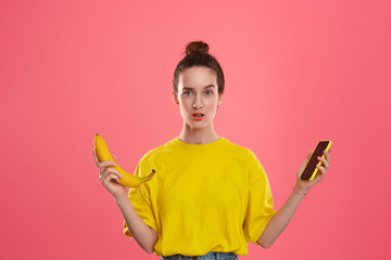 Model with a hair bun in a yellow t-shirt holding banana and yellow smartphone