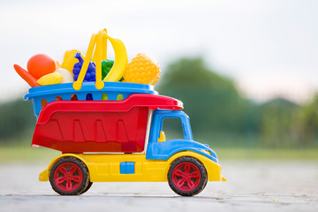 Bright plastic colorful toy car truck carrying basket with toy fruits and vegetables outdoors on...