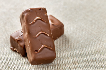Two isolated isolated dark brown chocolate candy snickers bars on light canvas cloth copy space background. Tasty food, nutritious, snack concept.