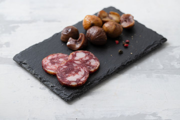 typical spanish smoked sausage salchichon and  boiled chestnuts on black board