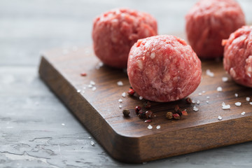 raw meatballs with pepper and salt on wooden board