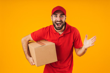 Portrait of excited delivery man in red uniform smiling and holding packaging box