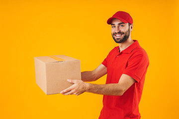 Image of satisfied delivery man in red uniform smiling and holding packaging box