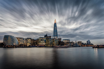 Fototapeta na wymiar Die markante Skyline von London an der Themse mit den beleuchteten Wolkenkratzern am Abend mit Wolken, Großbritannien