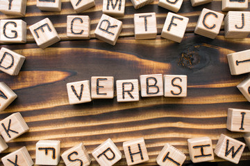 word verbs composed of wooden cubes with letters, Part of speech concept scattered around the cubes random letters, top view on wooden background