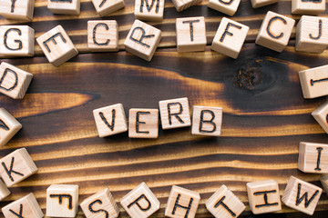 word verb composed of wooden cubes with letters, Part of speech concept scattered around the cubes random letters, top view on wooden background