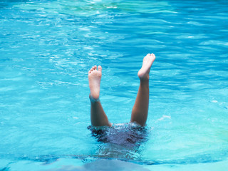 Active Boy diving and raising feet in the air at outdoor swimming pool