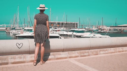 Tourist woman with straw sunhat looking to the mediterranean sea and enjoying the blue and scenic Denia marina Port , Alicante, Spain. Teal and orange style. - Powered by Adobe