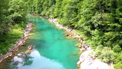 Flight of a quadcopter over a mountain's river canyon. We see the clear, transparent water of the river, it has the emerald color, the trees growing along the coast, and the mountains of Montenegro