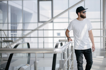 Hipster handsome male model with beard wearing white blank t-shirt and a baseball cap with space for your logo or design in casual urban style