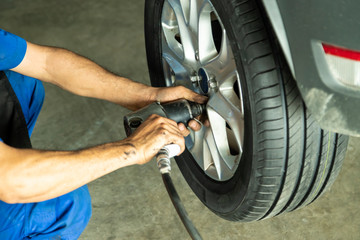 Mechanic changing car wheel with impact wrench at service shop.