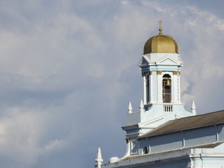 Rear view of a church tower with bells. The dome of the tower is golden and has a cross on its top. Cloudy winter sky.
