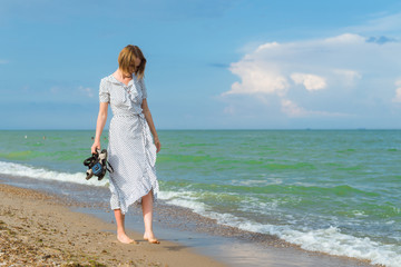 A woman in a dress walks along the seashore. Freedom, vacation concept.