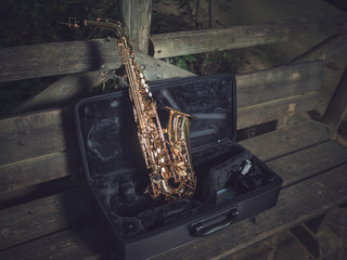 Illuminated saxophone, supported in his suitcase and on a bench in the park.