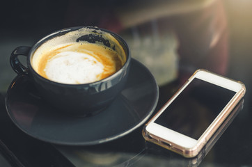 coffee cup and smartphone on table in coffee shop on morning in holiday technology communication concept.