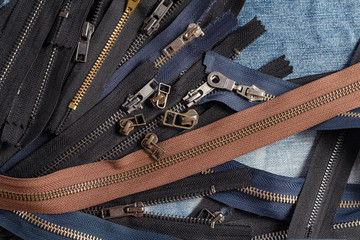 Pack a lot of black brown metal brass zippers stripes with sliders pattern for handmade sewing tailoring leatherwork leathercraft on the blue wooden background