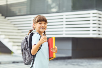 Smiling girl schoolgirl with a backpack in hand goes to school.