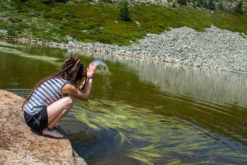 young woman with dreadlocks throws water on a rock in a lake in the mountain