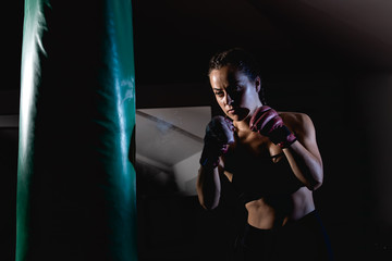 Young female boxer punching a bag on a sports training in a gym.