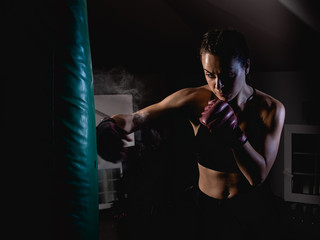 Young female boxer punching a bag on a sports training in a gym.