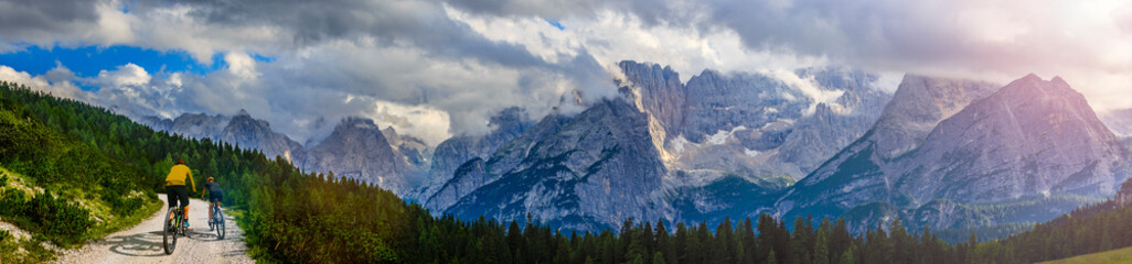 Cycling woman and man riding on bikes in Dolomites mountains andscape. Couple cycling MTB enduro...