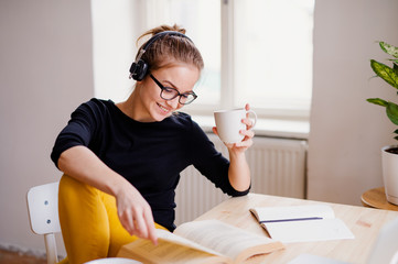 A young female student sitting at the table, using headphones when studying.
