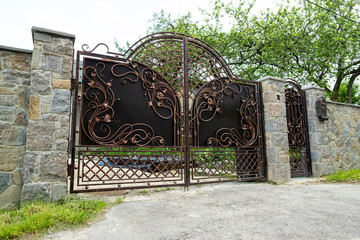 forged metal gates with patterns and a gate in a stone fence