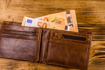 Brown leather wallet with fifty euro banknotes on the wooden background. Top view