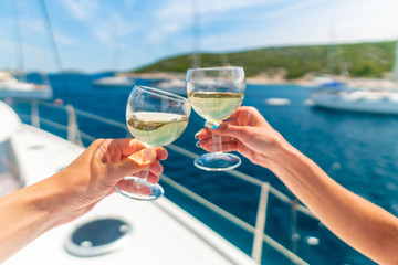 Couple holding two glasses of white wine over ocean background with yacht on background