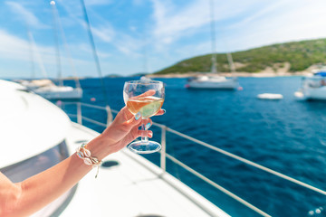 Woman holding glass of white wine over ocean background with yacht on background