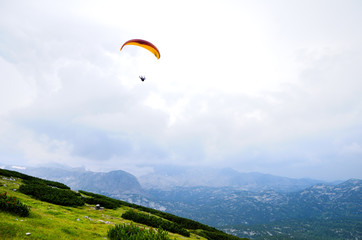 Paraglider flying over mountains in summer day.