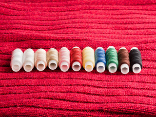Sewing still life spools of thread on background of red wool fabric