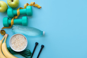 Fitness concept - apples, water, nuts, dumbbells and skipping rope on blue background. Copy space