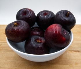 Fresh plums on white dish, wooden table, white background