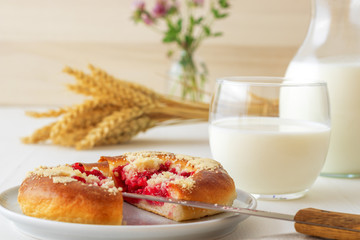 White table with yeasty sweet pastry with fresh currants and raspberries and streusel topping, glass and pitcher of milk, sheaf of wheat, small glass vase with flowers. Summer fresh fruit appetizer.