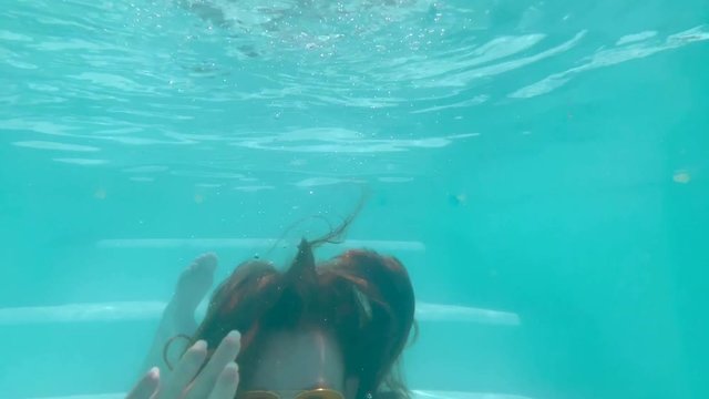 Redhead woman in blue swimming pool with yellow sunglasses