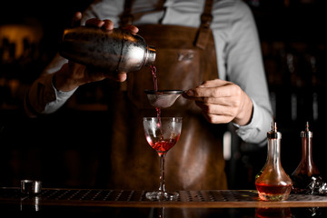 Fototapeta na wymiar Bartender flowing cocktail through sieve in glass