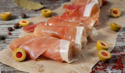 Closeup of thin slices of prosciutto with mixed olives and paprika on wooden cutting board