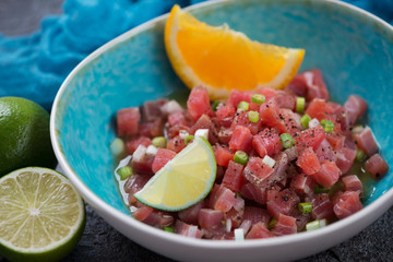 Closeup of tuna ceviche with lime and orange juice served in a turquoise bowl, studio shot