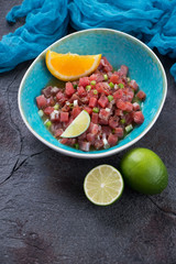 Turquoise bowl with tuna ceviche on a dark grey stone background, vertical shot, elevated view