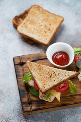Sandwich with grain bread, chicken fillet, cheese and vegetables, elevated view over beige stone background, studio shot