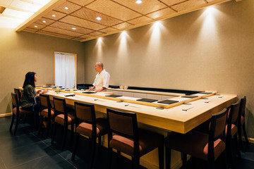 Japanese Omakase Restaurant that decorated mostly with wood. Chef cooking in kitchen counter and...