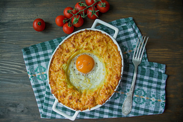 Potato casserole with bolognese. Baked potato casserole with egg and grated cheese in a ceramic oval baking sheet. Wooden dark background.