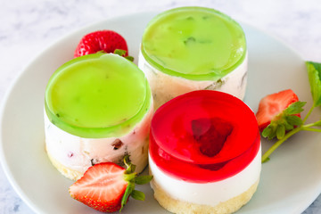 Mini round cold cheesecakes with fruit jelly and strawberries.