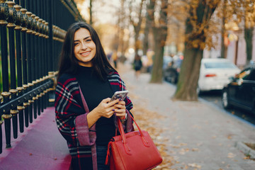 Naklejka premium girl using her cell phone while walking through the park during autumn