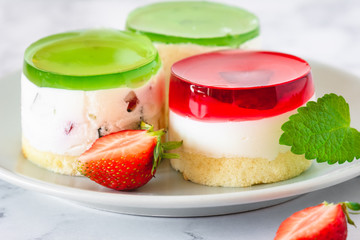 Mini round cold cheesecakes with fruit jelly and strawberries.