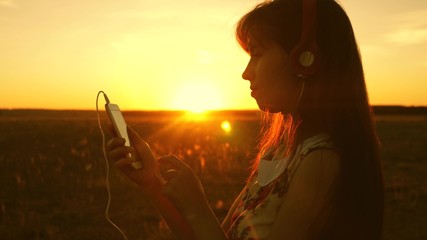 girl listening to music and dancing in the rays of a beautiful sunset. young girl in headphones and...