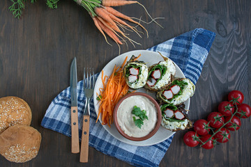Zucchini roll with crab sticks, eggs and spinach. Delicious appetizer served on a round plate with sauce and fresh vegetables and herbs. View from above.