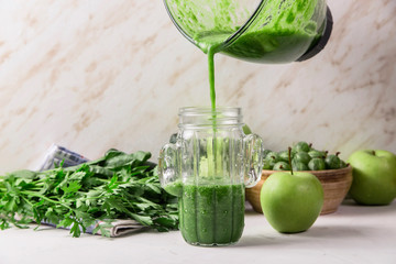 Green smoothies are poured from a glass blender bowl into a glass in the shape of a cactus. Healthy...